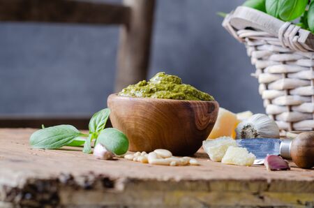 Pesto sauce in a olive wooden bowl with pine nuts, basil, parmesan and garlic over rustic table.の写真素材