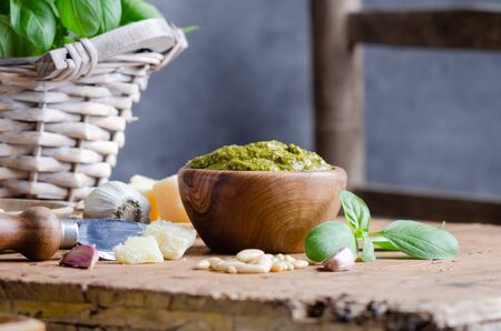 Pesto sauce in a olive wooden bowl with pine nuts, basil, parmesan and garlic over rustic table.の写真素材
