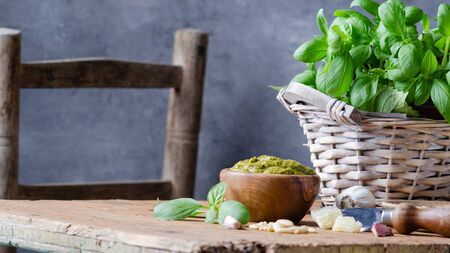 Pesto sauce in a olive wooden bowl with pine nuts, basil, parmesan and garlic over rustic table.の写真素材