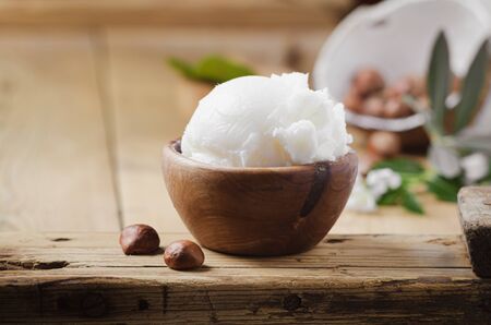 Shea butter in wooden bowl with nuts on old rustic table. Free text space.の写真素材