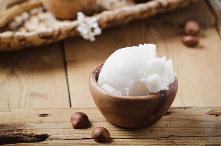 Shea butter in wooden bowl with nuts on old rustic table. Free text space.の写真素材