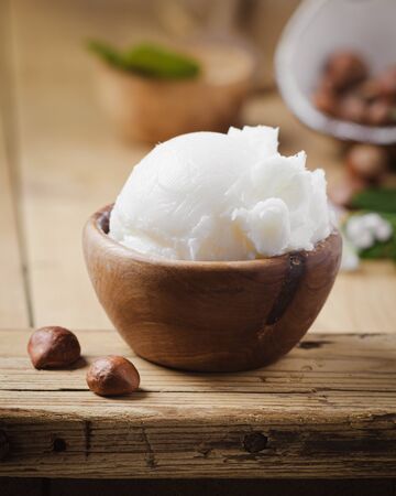 Shea butter in wooden bowl with nuts on old rustic table. Free text space.の写真素材