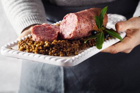 Female hands holding white plate with Italian large pork sausage cotechino served with lentils.の写真素材