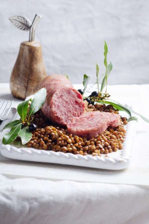 Italian large pork sausage cotechino served with lentils on white plate.の写真素材