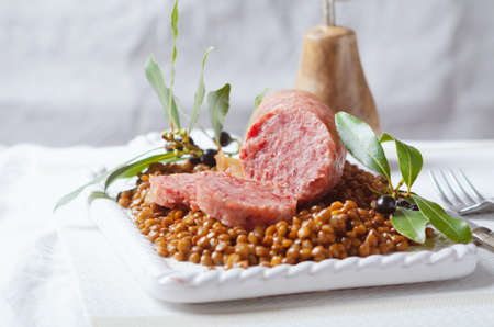 Italian large pork sausage cotechino served with lentils on white plate.の写真素材
