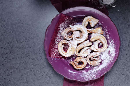 Italian carnival fritters galeno glove dusted with polwered sugar served on purple plate.の写真素材