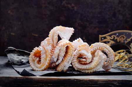 Italian carnival fritters galeno glove dusted with polwered sugar served on black wooden board.の写真素材