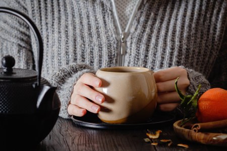 Close-up of hands holding cup of dark tea with orange, cinnamon, anise and cloves. Winter's Day, cozy time and winter drinks.の写真素材