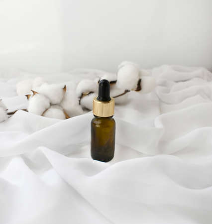 Essential oil   bottle dropper, cotton flowers on silk background. Delicate luxury spa aromatherapy or bodycare concept. Elegant design for cosmetics branding, beauty blogging or natural skincare productの写真素材