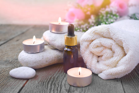 Aromatherapy concept with essential oil bottle, towel, burning candles and pebbles. Spa or herbal...