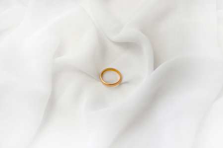 Elegant wedding concept. Golden bridal ring on white silk background. Feminine still life...