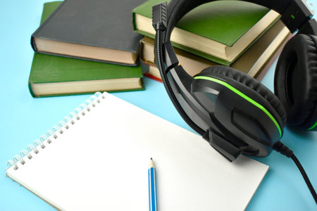 Modern education concept with close up headphones and stack of books, empty notepad. Audiobook....