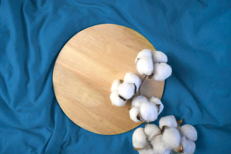 Empty wooden plate with cotton flowers on blue fabric background. Eco friendly treatment. Mock up minimalist setting. Flat lay. Top view.の写真素材