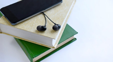 Close up earphones, tablet on stack of books. Listening to book. Audio book concept. Online...