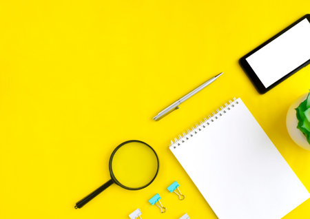 Smartphone, magnifying glass, notebook and succulent on yellow background. Job searching or distance...