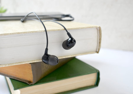 Close up earphones and stack of books on desk. Audiobook concept Modern education listening to book....
