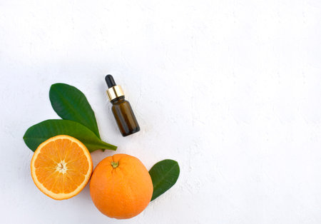 Trendy minimalist flatlay with fresh orange, essential oil bottle and leaves on white background....