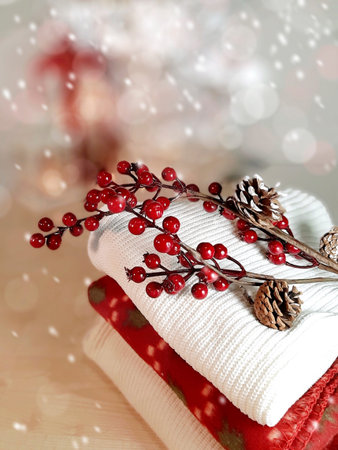 Cloth pile with red berries branch on snowy bokeh background. Christmas or wintertime hygge concept....