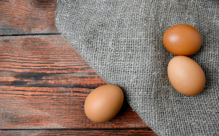 Brown eggs, sack fabric on wooden background. Easter minimalist or healthy eating concept. Copy...