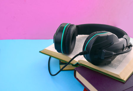 Audio book concept. Close up headphones, open book and pile of books on colored background. Listening to book. Modern education. Copyspace.の写真素材