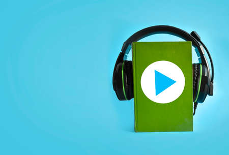 Audio book concept with headphones, green book on blue background. E-learning. Start playing button. Copyspace.の写真素材