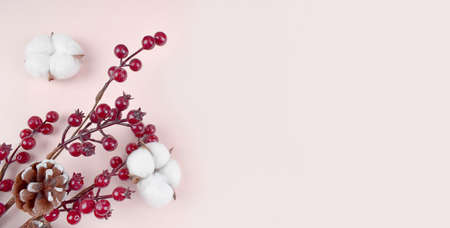 Happy Christmas composition with red berries and cotton flowers on pastel background. Greeting minimalist concept for winter holidays. New year 2021. Banner.の写真素材