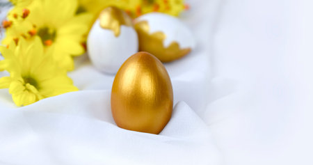 Close up Happy Easter concept with golden decorated egg, yellow flowers on white silk fabric....