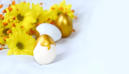 Close up Happy Easter concept with golden decorated egg, yellow flowers on white silk fabric....