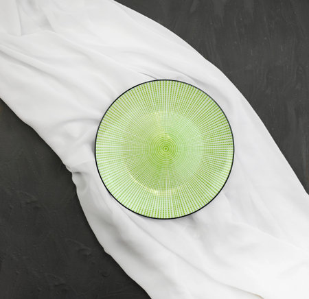 Empty ceramic plate with white silk fabric on black textured background. Elegant minimalist wedding table setting. Linen ornamental dish. Top view.の写真素材