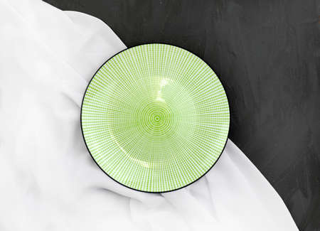 Empty ceramic plate with white silk fabric on black textured background. Elegant minimalist wedding table setting. Linen ornamental dish. Top view.の写真素材