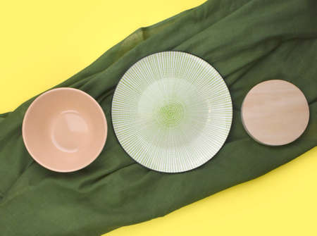 Mock up row of ceramic table ware with green fabric on yellow background. Minimalist summer kitchen setting. Eco friendly style. Trendy color design. Top view. Flat lay.の写真素材