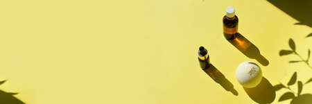 Mock up spa aromatherapy composition with essential oil bottle, dropper, bath bomb on yellow background. Trendy minimal concept of organic cosmetics, skin and body care. Hard light and shadow.の写真素材