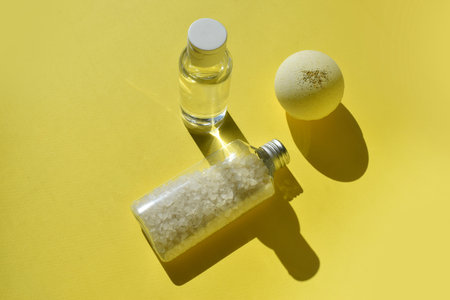 Minimal spa concept with lotion gel, bath bomb and sea salt on yellow background. Summertime bathe...