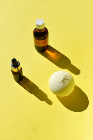 Spa aromatherapy composition with essential oil bottle, dropper, bath bomb on yellow background. Trendy minimal concept of organic cosmetics, skin and body care. Wellnessの写真素材