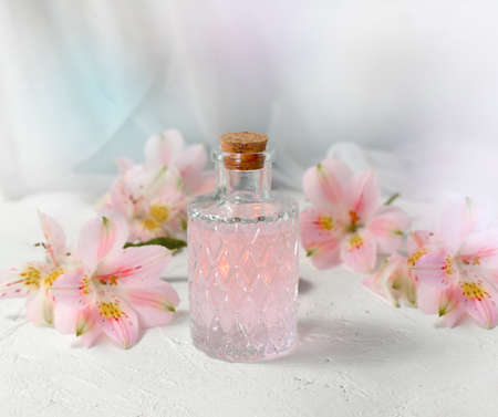 Beautiful perfume or aromatic oil glass with flowers over light background. Close up composition for spa, aromatherapy or massage. Relaxation. Wellness. Natural organic cosmetics.の写真素材