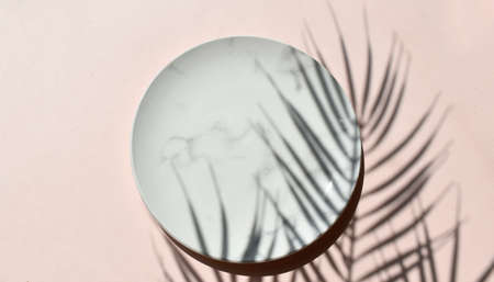 Mockup empty marble plate on neutral beige background. Summer minimal tableware composition. Palm leaves shadow. Elegant concept for wedding invitation, restaurant menu or spa branding.の写真素材