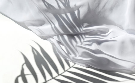 Summer sunlight still life mock up composition. White silk fabric on table in sunlit background. Palm leaves harsh shadows. Luxury minimal concept for wedding, resort vacation or spa products.の写真素材