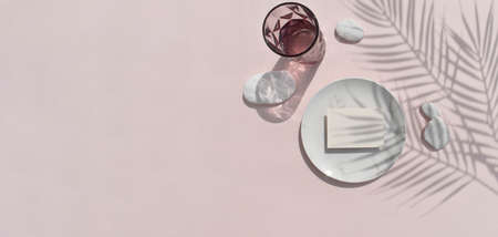 Mock up tropical still life mockup composition. Blank invitation card, marble plate with sea pebbles on beige background. Harsh palm shadows, reflection. Banner for wedding invitation or business.の写真素材