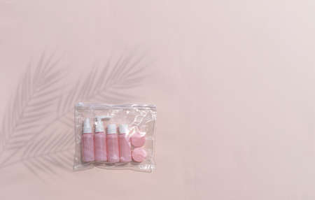 Mock up feminine flatlay with small size cosmetic bottles in traveling bag on neutral pastel background. Palm leaves shadows. Minimal skin or body care products concept for vacation or journey.の写真素材