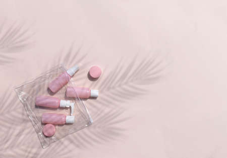 Mock up feminine flatlay with small size cosmetic bottles in traveling bag on neutral pastel background. Palm leaves shadows. Minimal skin or body care products concept for vacation or journey.の写真素材
