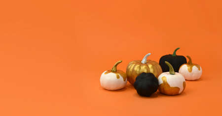 Halloween minimal creative still life. Golden and black pumpkins on orange background. Seasonal greeting mock up banner for fall, Thanksgiving or Halloween sale. Trendy autumn layout concept.の写真素材