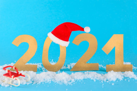Christmas 2021, number in the snow with sledges and hat on blue background.