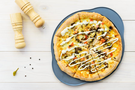 Pizza with chicken, tomatoes, pepper, cheese and sauce on a light wooden table. Horizontal...