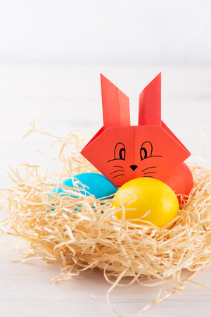 Paper rabbit in a nest with colored eggs. Easter concept.