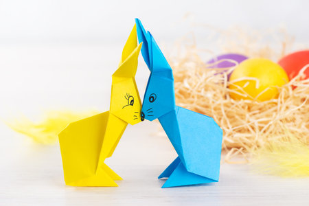 Origami hares from colored paper on the background of eggs in the nest. Easter concept.