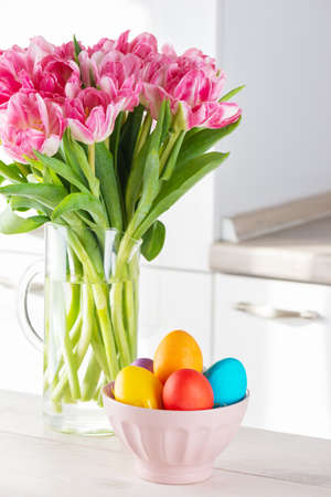 Painted Easter eggs in a bowl with a bouquet of tulips.の写真素材