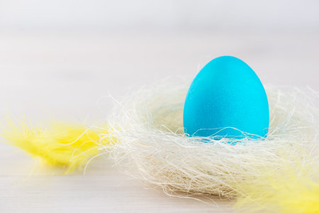 Blue Easter egg in a nest with feathers on a wooden table.