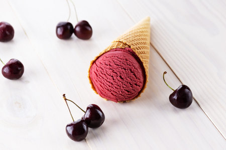 Cherry ice cream in a cone on a wooden table.