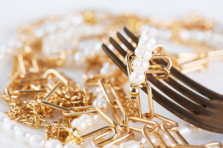 Jewelry bijouterie gold chain and pearl necklace on a fork, close-up. Shopaholism, waste of money,...