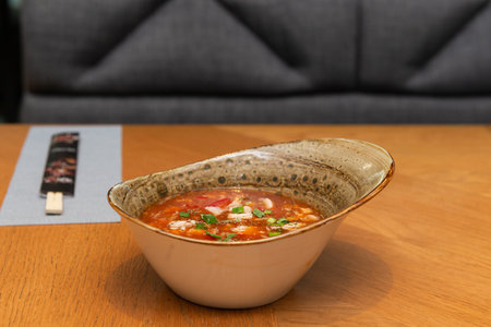 Spicy tomato soup with chicken, green onions, chili peppers and herbs in a restaurant, Asian cuisine. Tom yum soup with chicken.の写真素材